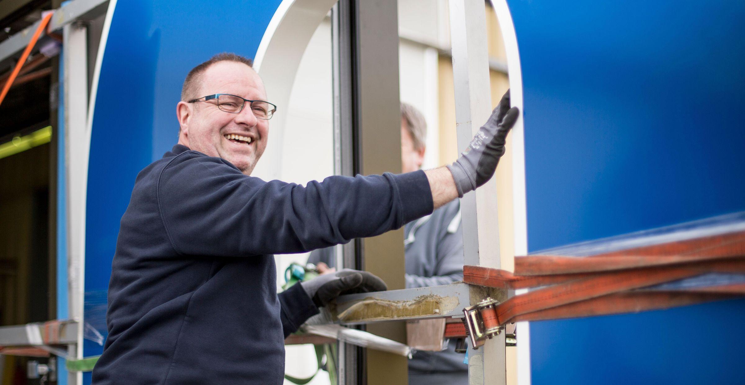 Lächelnder Metallbauer montiert Fenster in einer Baustelle, trägt Arbeitskleidung und Schutzhandschuhe.