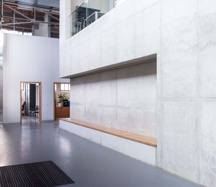 Moderne Betonwand mit integrierter Holzbank im Innenbereich eines sanierten Industriegebäudes.