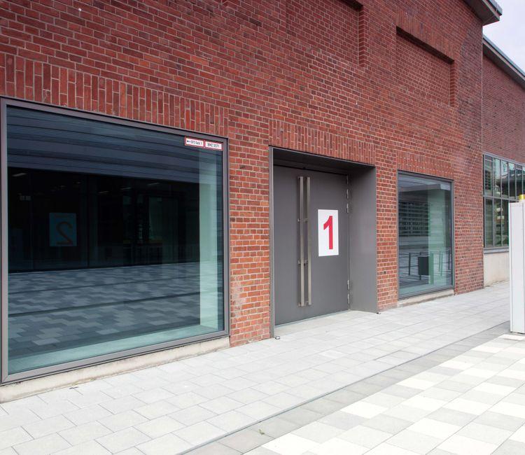 Großzügige Platzgestaltung vor einem Backsteinbau mit Glasfassade