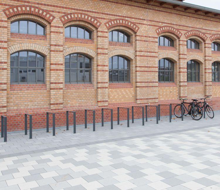 Fahrradständer vor der rot-gelben Backsteinfassade mit symmetrisch angeordneten Fenstern.