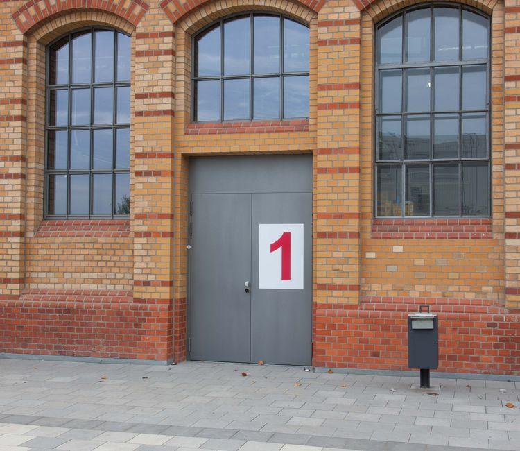 Doppelflügelige Eingangstür mit der Markierung „1“ im historischen Ziegelbau.