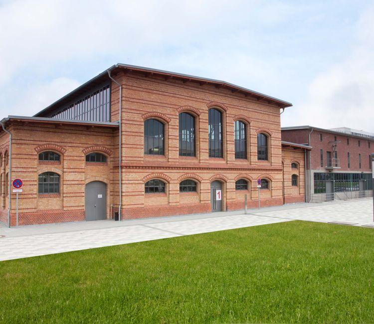Weitwinkelansicht des Gebäudekomplexes mit altem Ziegelbau und moderner Erweiterung.