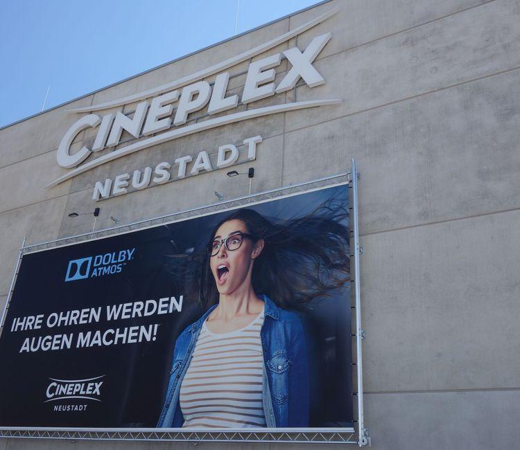 Großes Cineplex-Wandlogo in Neustadt über einem Werbebanner mit Dolby Atmos-Ankündigung.
