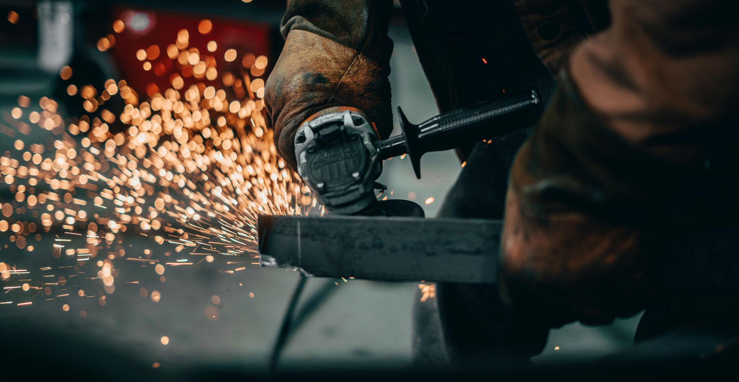Ein Handwerker mit Schutzhandschuhen bedient eine Winkelschleifmaschine, um Metall zu schneiden, wodurch Funken sprühen.