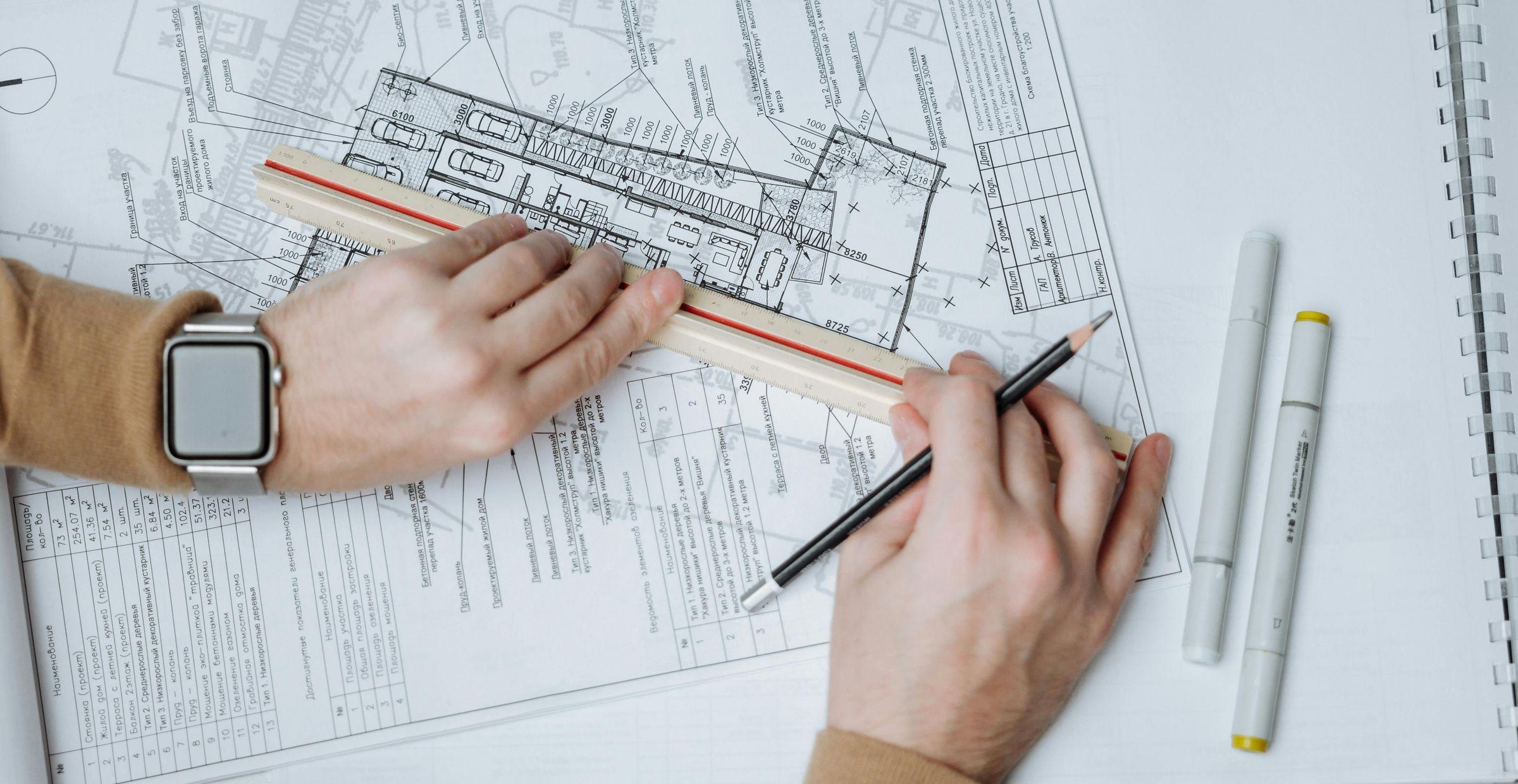 Person überprüft und markiert architektonische Pläne mit einem Bleistift und Lineal, Details auf einem Bauplan hervorhebend.
