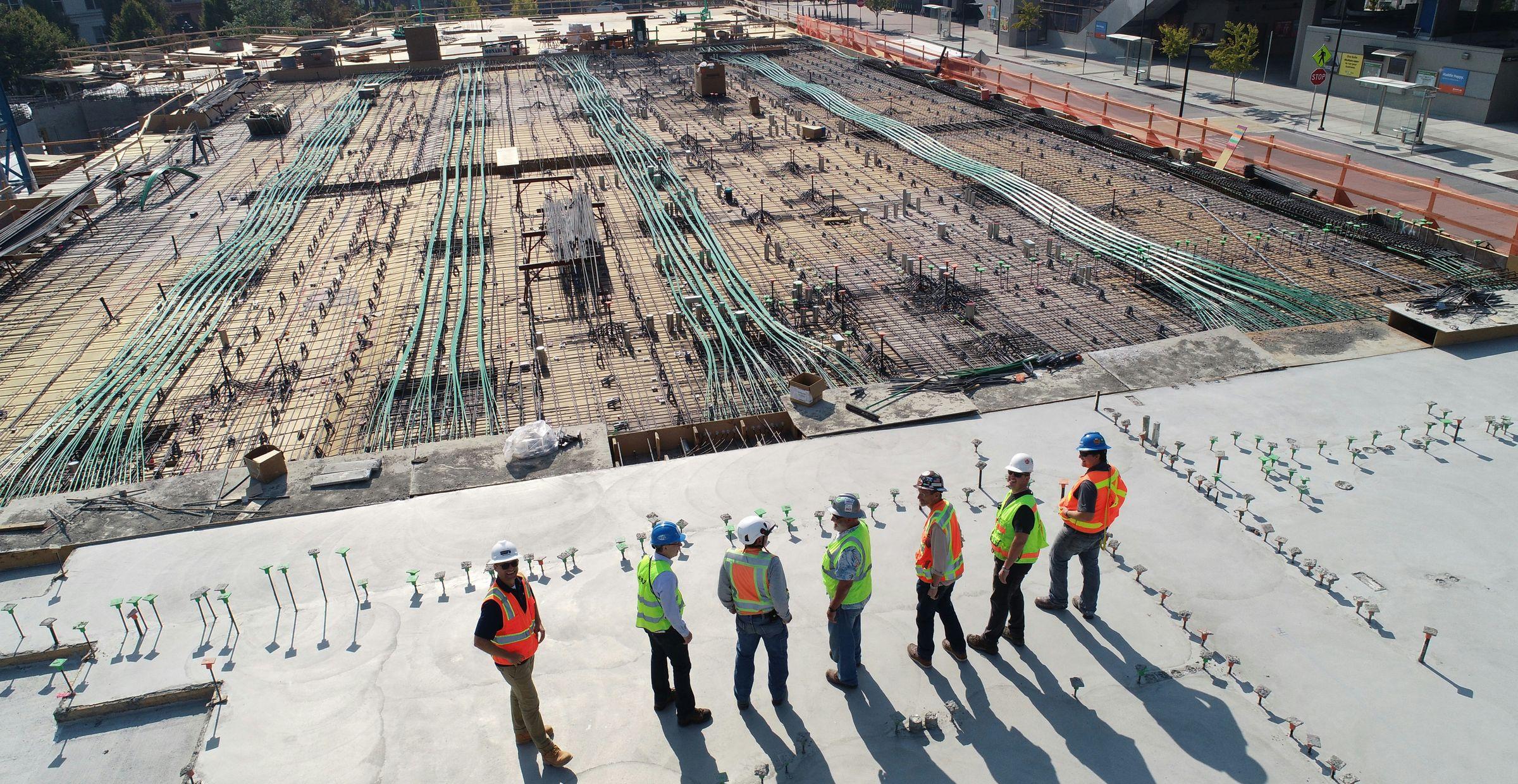 Gruppe von Bauarbeitern in Schutzausrüstung steht auf einer großen Baustelle, die mit Stahlverstärkungen für einen Betonguss vorbereitet ist.
