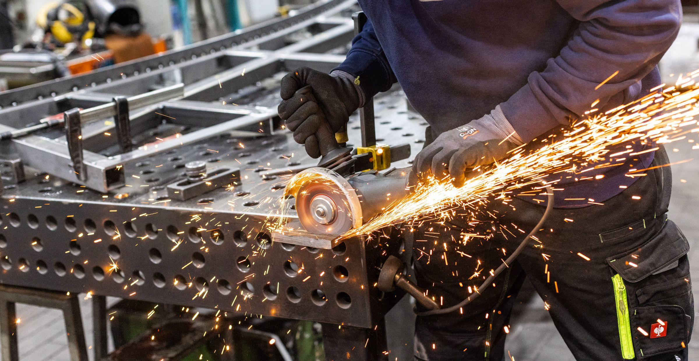Detailaufnahme von Person in Arbeitskleidung, die Metallplatte schleift, Funken fliegen.